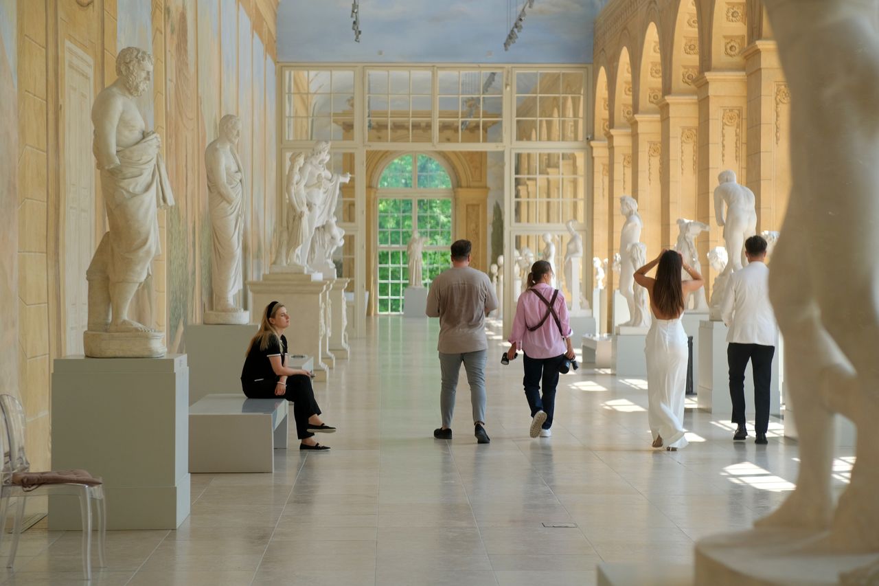 Visitors admire classical sculptures in a sunlit museum corridor, capturing art appreciation.